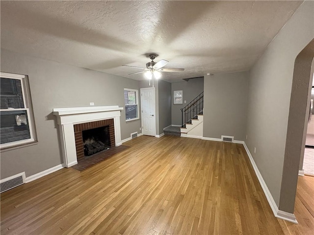 unfurnished living room featuring a fireplace, ceiling fan, hardwood / wood-style floors, and a textured ceiling