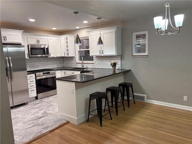 kitchen with white cabinetry, light wood-type flooring, decorative light fixtures, and appliances with stainless steel finishes