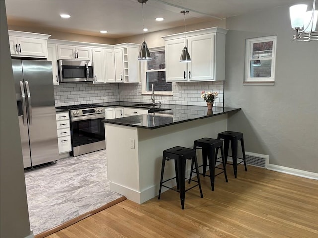 kitchen featuring decorative light fixtures, light wood-type flooring, white cabinetry, and appliances with stainless steel finishes