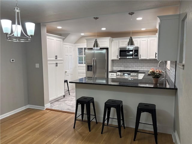 kitchen featuring appliances with stainless steel finishes, decorative light fixtures, an inviting chandelier, light hardwood / wood-style flooring, and white cabinetry