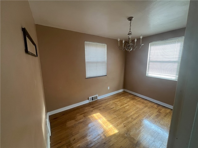 spare room with hardwood / wood-style flooring and an inviting chandelier