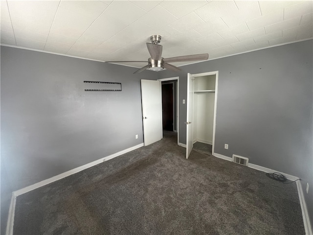 unfurnished bedroom featuring ceiling fan, a closet, crown molding, and dark colored carpet