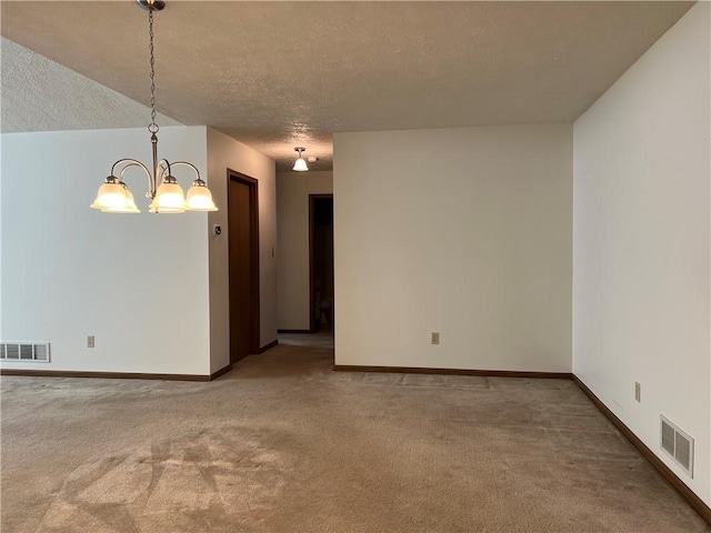 carpeted empty room featuring a textured ceiling and an inviting chandelier