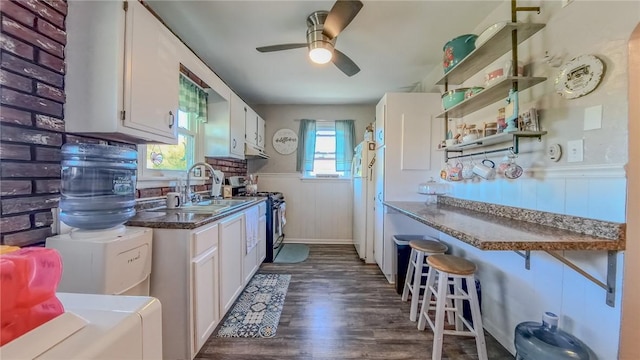 kitchen featuring a kitchen breakfast bar, dark hardwood / wood-style flooring, stainless steel gas range oven, ceiling fan, and white cabinetry