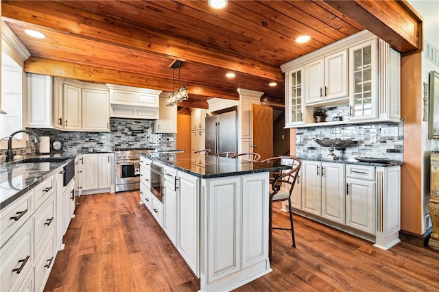 kitchen featuring dark hardwood / wood-style flooring, high end appliances, dark stone countertops, a kitchen island, and hanging light fixtures