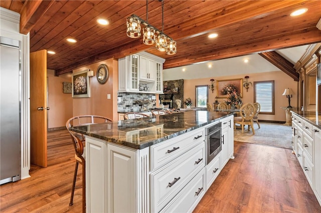 kitchen with wood ceiling, hardwood / wood-style flooring, dark stone countertops, white cabinetry, and an island with sink