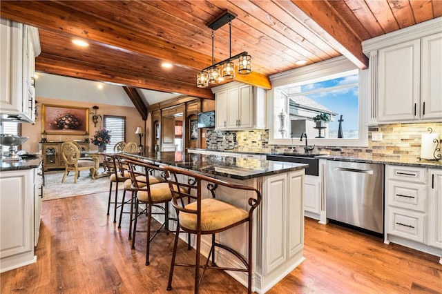 kitchen featuring stainless steel dishwasher, white cabinetry, a breakfast bar area, and beamed ceiling