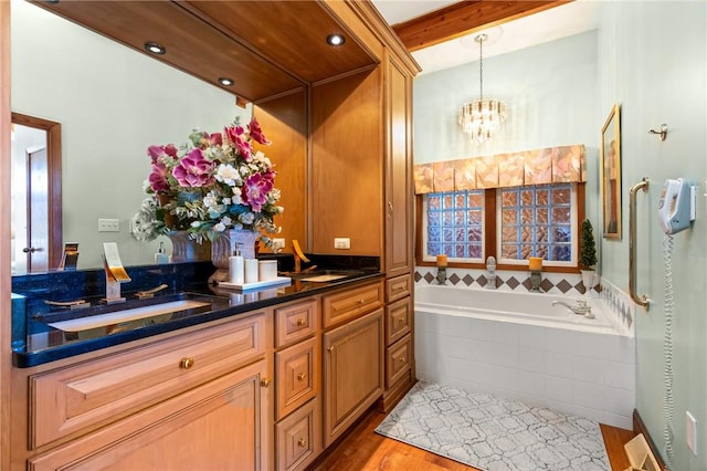 bathroom featuring beam ceiling, a notable chandelier, tiled tub, wood-type flooring, and vanity