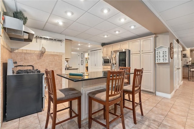 kitchen with stainless steel appliances, a kitchen breakfast bar, kitchen peninsula, light tile patterned floors, and ornamental molding