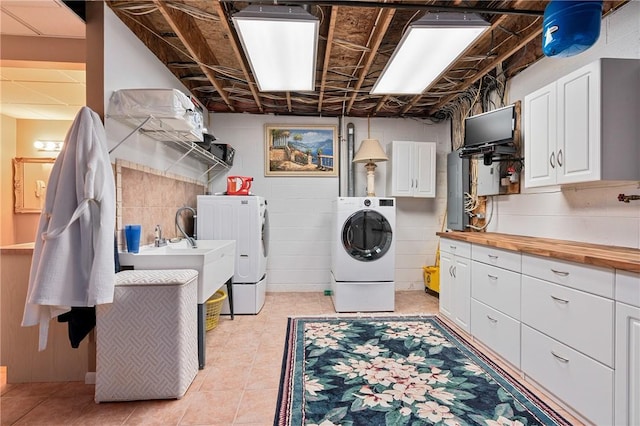 clothes washing area with cabinets, light tile patterned floors, washing machine and dryer, and sink