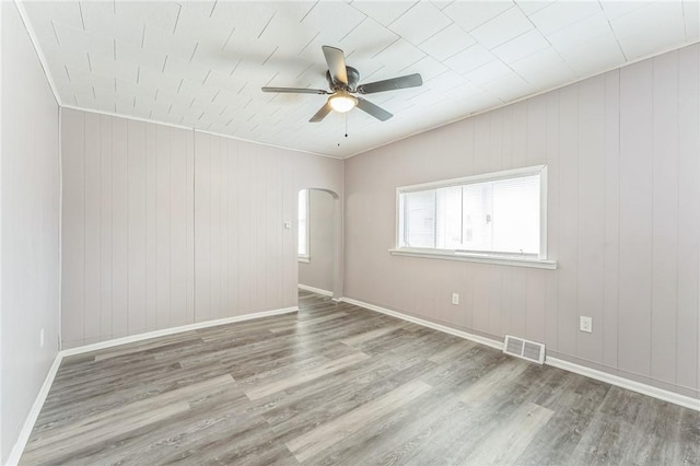 empty room with hardwood / wood-style flooring, ceiling fan, and wooden walls