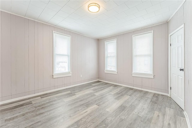 unfurnished room featuring wood walls, plenty of natural light, and light hardwood / wood-style floors