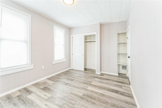 unfurnished bedroom featuring a closet, wooden walls, and light hardwood / wood-style flooring