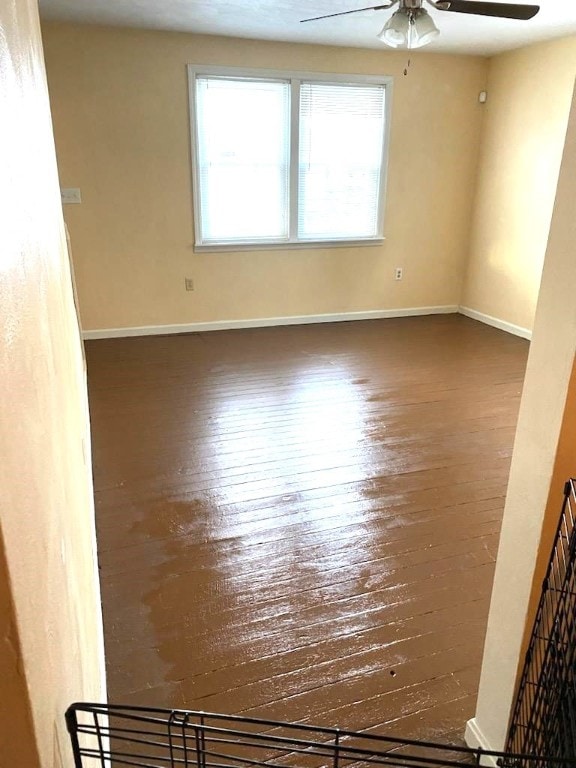 empty room featuring baseboards, wood-type flooring, and a ceiling fan