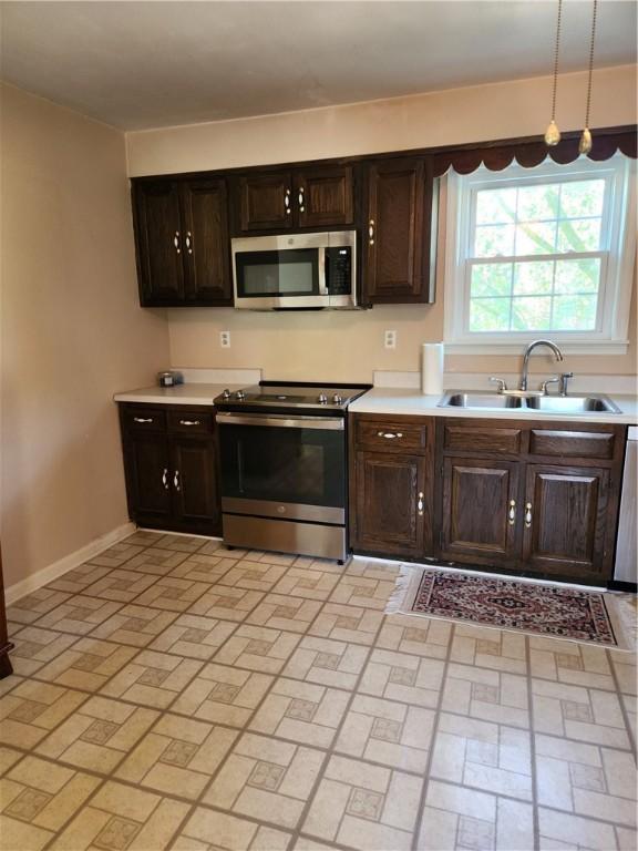 kitchen with brick patterned floor, baseboards, light countertops, a sink, and appliances with stainless steel finishes
