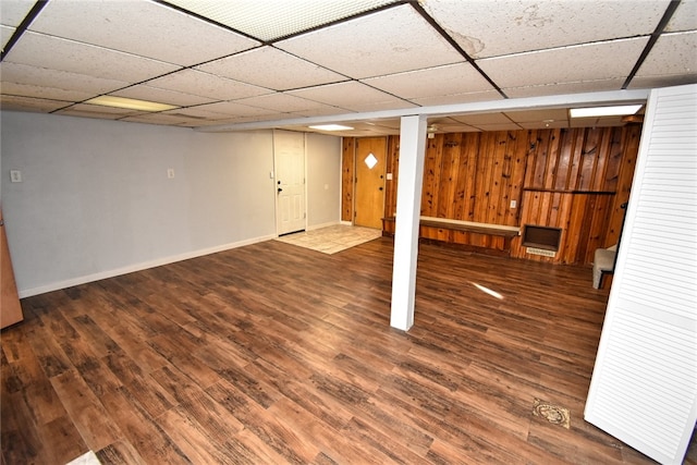 basement featuring wood-type flooring, a paneled ceiling, and wood walls