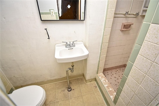 bathroom featuring a tile shower, tile patterned floors, sink, and toilet