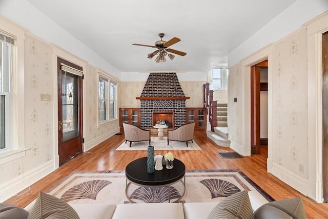 living room featuring ceiling fan, light wood-type flooring, a wealth of natural light, and a brick fireplace