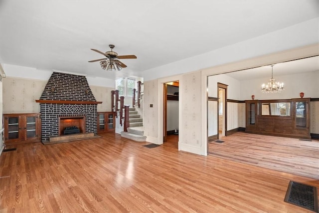 unfurnished living room with ceiling fan with notable chandelier, light hardwood / wood-style floors, and a brick fireplace