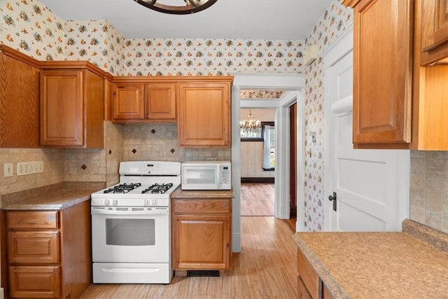 kitchen featuring decorative backsplash, light hardwood / wood-style flooring, white appliances, and an inviting chandelier