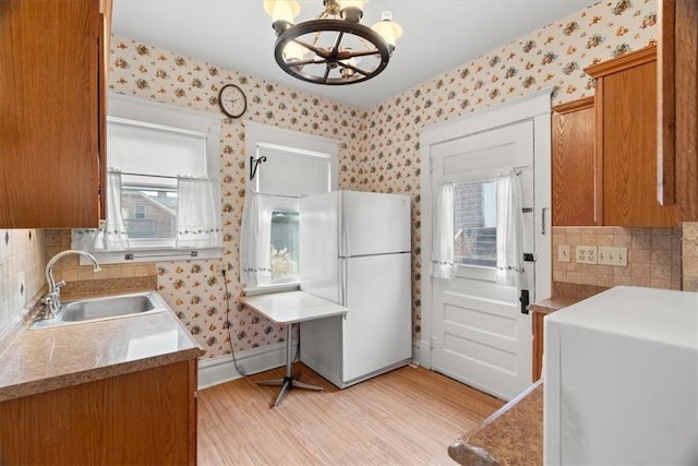 kitchen with an inviting chandelier, sink, light wood-type flooring, decorative light fixtures, and white fridge