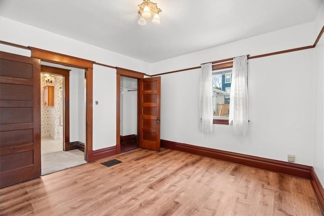 unfurnished bedroom featuring ensuite bathroom, light hardwood / wood-style flooring, and a closet