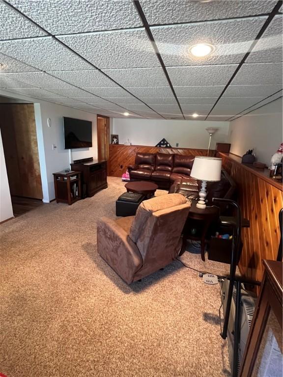 carpeted living room featuring a drop ceiling and wood walls