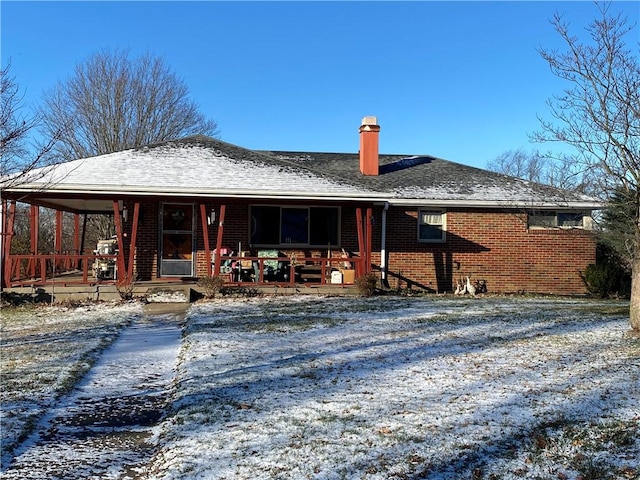 snow covered back of property featuring covered porch