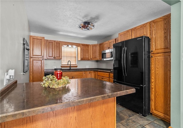 kitchen featuring black refrigerator, a textured ceiling, kitchen peninsula, and sink