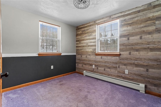 carpeted empty room with baseboard heating, wood walls, and a healthy amount of sunlight