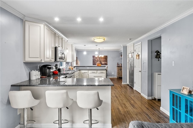 kitchen with kitchen peninsula, appliances with stainless steel finishes, a kitchen bar, pendant lighting, and dark hardwood / wood-style floors