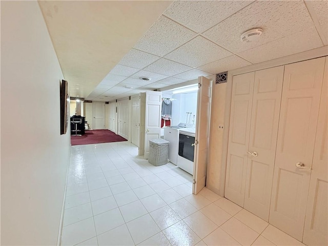 hallway with light tile patterned floors, washer / clothes dryer, and a drop ceiling