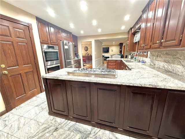 kitchen featuring light stone countertops, sink, kitchen peninsula, decorative backsplash, and appliances with stainless steel finishes