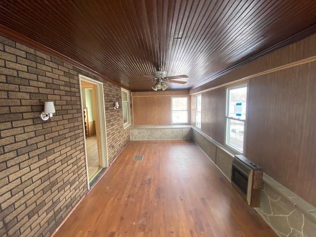 interior space featuring brick wall, heating unit, crown molding, wood-type flooring, and wooden ceiling