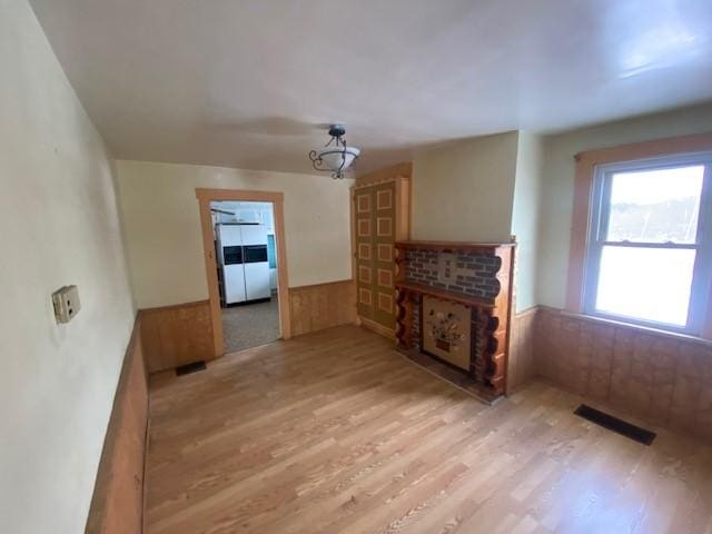 unfurnished living room featuring a fireplace, light hardwood / wood-style flooring, and wooden walls