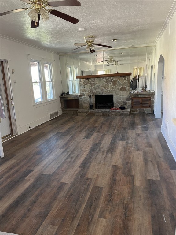 unfurnished living room featuring crown molding, dark hardwood / wood-style flooring, a stone fireplace, and a textured ceiling