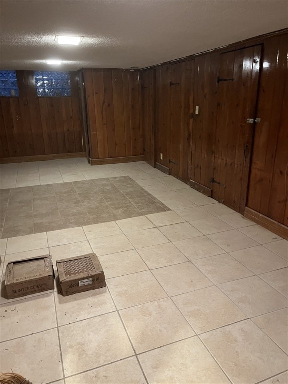 basement featuring wood walls, light tile patterned floors, and a textured ceiling