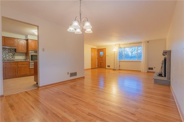 unfurnished living room featuring a fireplace, light wood-type flooring, and a notable chandelier