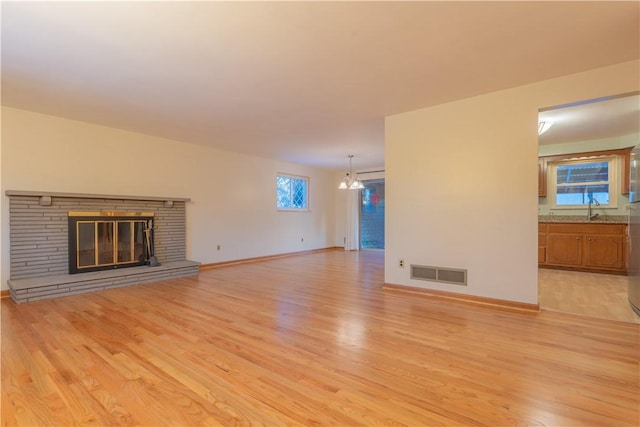 unfurnished living room with sink, a fireplace, an inviting chandelier, and light wood-type flooring