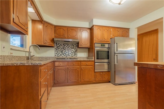 kitchen with appliances with stainless steel finishes, backsplash, light stone counters, sink, and light hardwood / wood-style floors