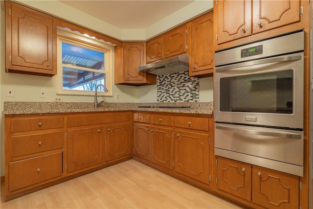 kitchen with backsplash, sink, light wood-type flooring, light stone counters, and stainless steel double oven