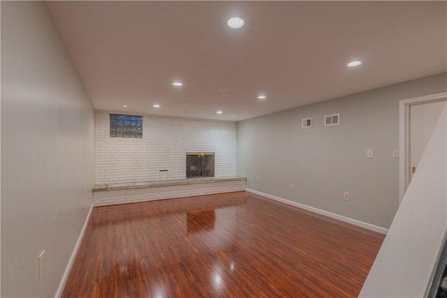 unfurnished living room featuring a fireplace, hardwood / wood-style floors, and brick wall