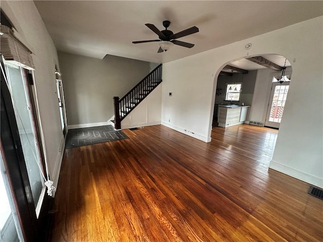 unfurnished living room with arched walkways, wood-type flooring, visible vents, baseboards, and stairs