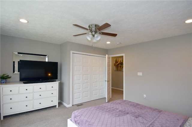 bedroom featuring ceiling fan, a closet, light carpet, and a textured ceiling