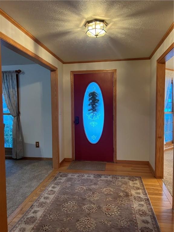 foyer with a textured ceiling, ornamental molding, and light wood-style flooring