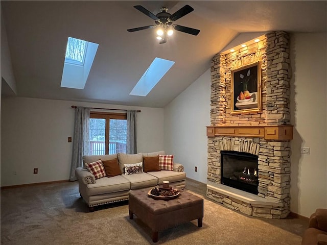 carpeted living area with baseboards, lofted ceiling with skylight, a ceiling fan, and a stone fireplace