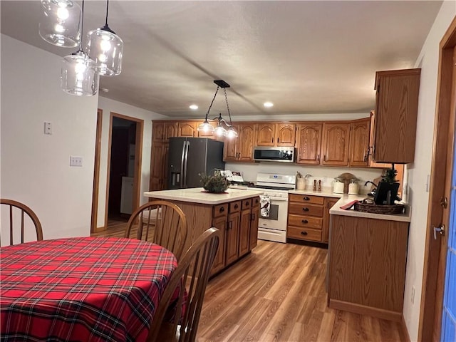 kitchen with light wood finished floors, white gas range, black fridge, brown cabinets, and stainless steel microwave