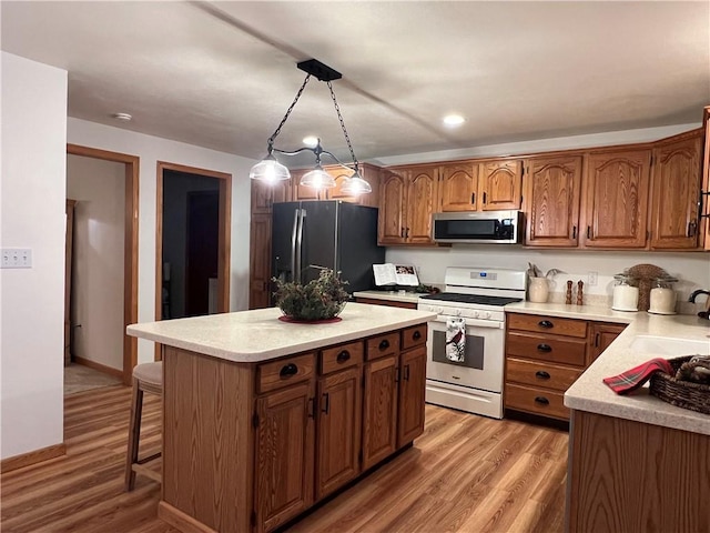 kitchen featuring white gas range, stainless steel microwave, a sink, brown cabinetry, and freestanding refrigerator