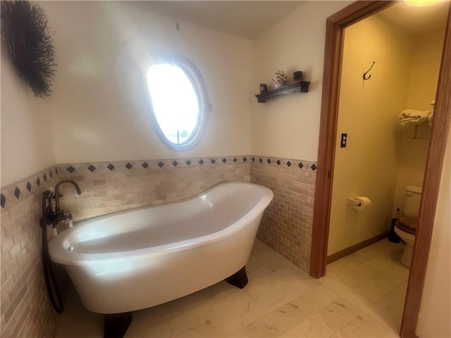 bathroom featuring tile walls, a wainscoted wall, toilet, and a freestanding bath