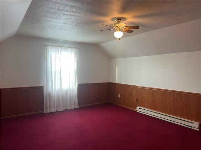 bonus room with dark carpet, lofted ceiling, ceiling fan, a textured ceiling, and baseboard heating